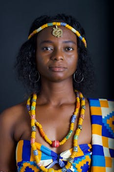 Elegant portrait of a woman in vibrant traditional Ghanaian clothing against a dark studio background.