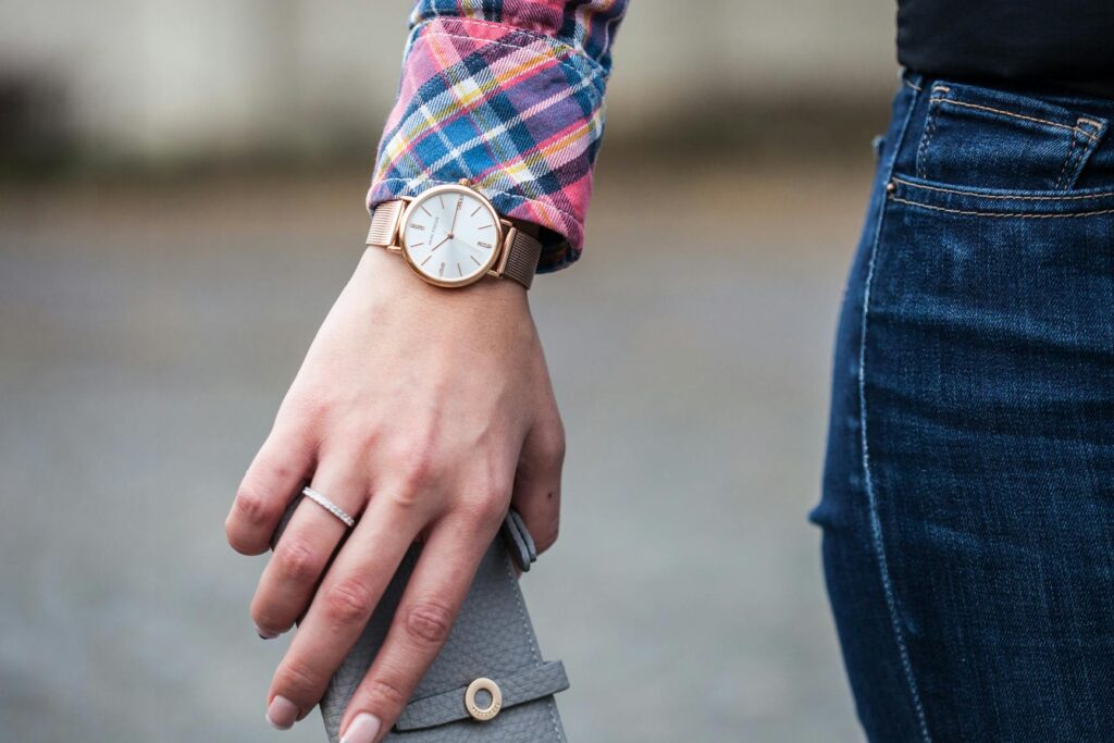 Close-up of a woman wearing a wristwatch and denim jeans, holding a clutch outdoors.